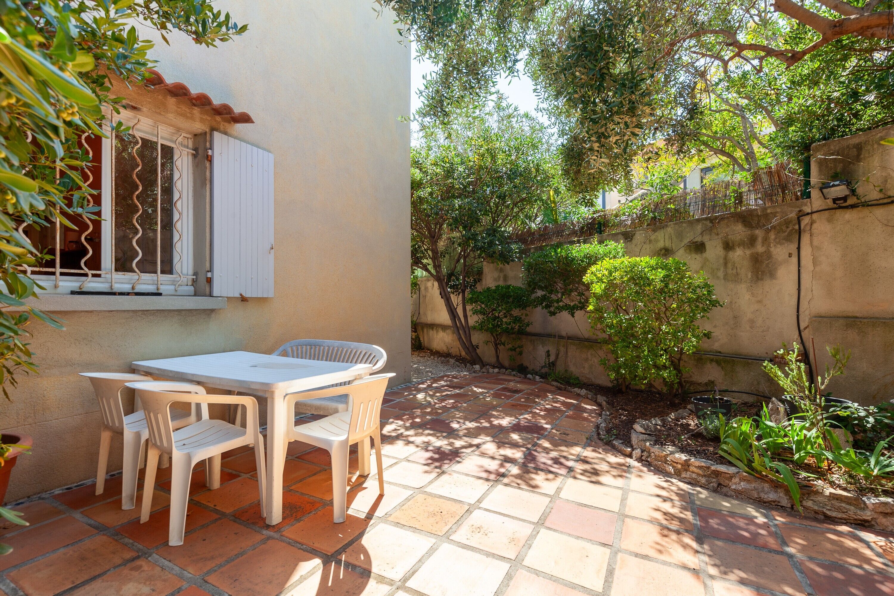 A patio with a table and chairs, a window with bars, and a garden with plants and a wall.