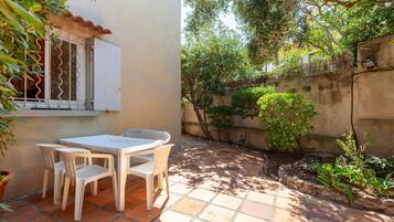 A patio with a table and chairs, a window with bars, and a garden with plants and a wall.
