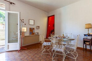Zona pranzo con tavolo in vetro, sedie bianche, una porta rossa e un termosifone.