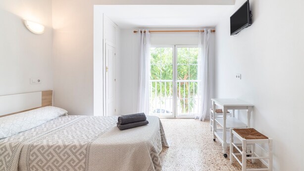 A bedroom with a bed, a TV, a window with curtains, and a white wall.
