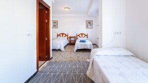 Ein Hotelzimmer mit zwei Einzelbetten, einer Holztür, einem kleinen Tisch und einer Deckenleuchte.