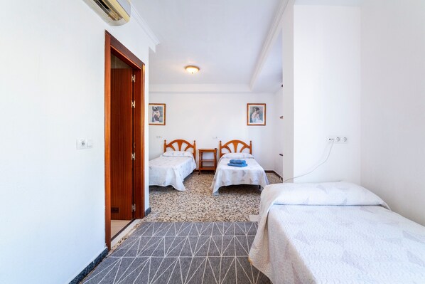 A hotel room with two single beds, a wooden door, a small table, and a ceiling light.