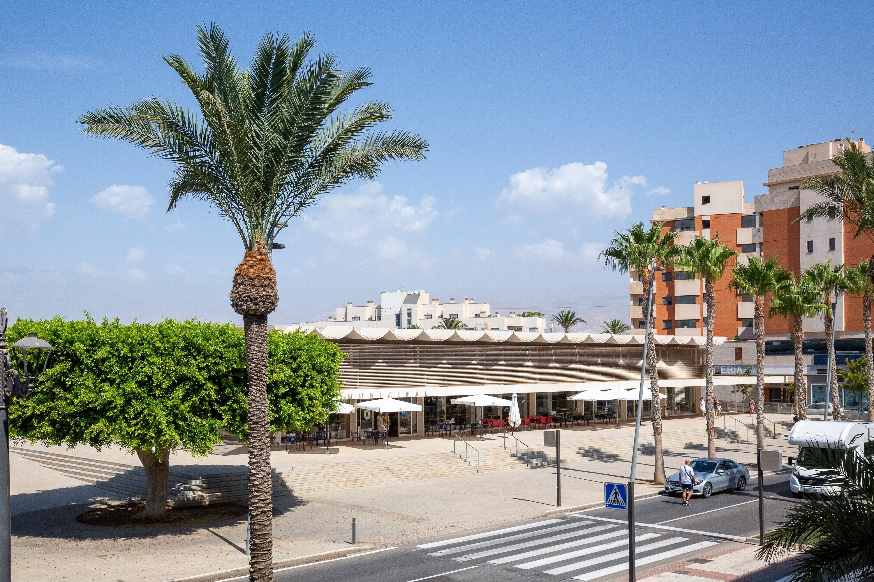 A hotel with outdoor seating, palm trees, and a clear sky.