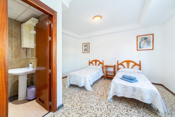 A bedroom with two beds, a wooden door, a sink, and a mirror.