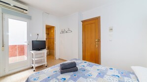 Un dormitorio con una cama, un televisor sobre un mueble, una puerta de madera y una ventana.