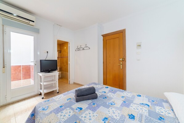 A bedroom with a bed, a TV on a stand, a wooden door, and a window.