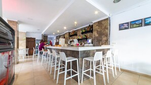 Zona de bar con mostrador, taburetes blancos y un área de estar con sillas.