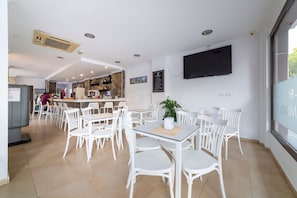 Un intérieur de restaurant moderne avec des chaises et des tables blanches, un bar et un téléviseur fixé au mur.