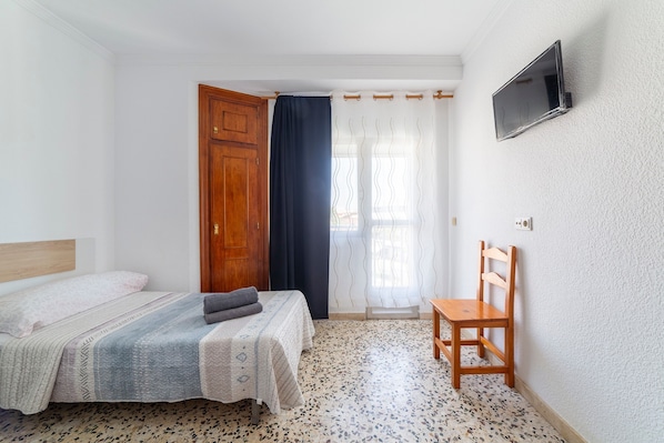 Une chambre à coucher avec un lit, une chaise, une télévision et une fenêtre avec des rideaux.