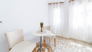 Une pièce avec une table ronde, deux chaises, un vase de fleurs et une fenêtre avec des rideaux.