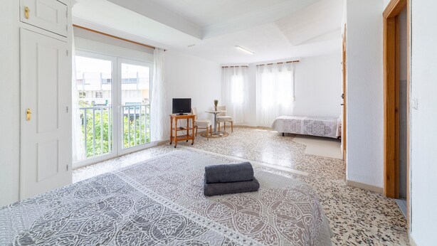 Une chambre d’hôtel avec un sol à motifs, un lit, une télévision, une petite table avec des chaises et un balcon avec vue.