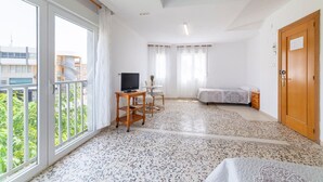 Une chambre avec un lit, un téléviseur posé sur un meuble, une petite table et un balcon doté d’une rambarde.