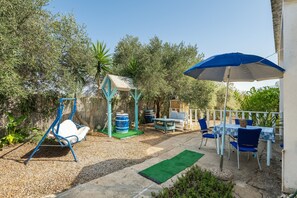 A patio with a swing set, a table with chairs, and a blue umbrella.