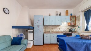 A compact kitchen with a dining area, a sofa, and a clock on the wall.