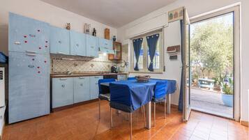 A kitchen with blue cabinets, a dining table with blue tablecloth, and a view of the outside.