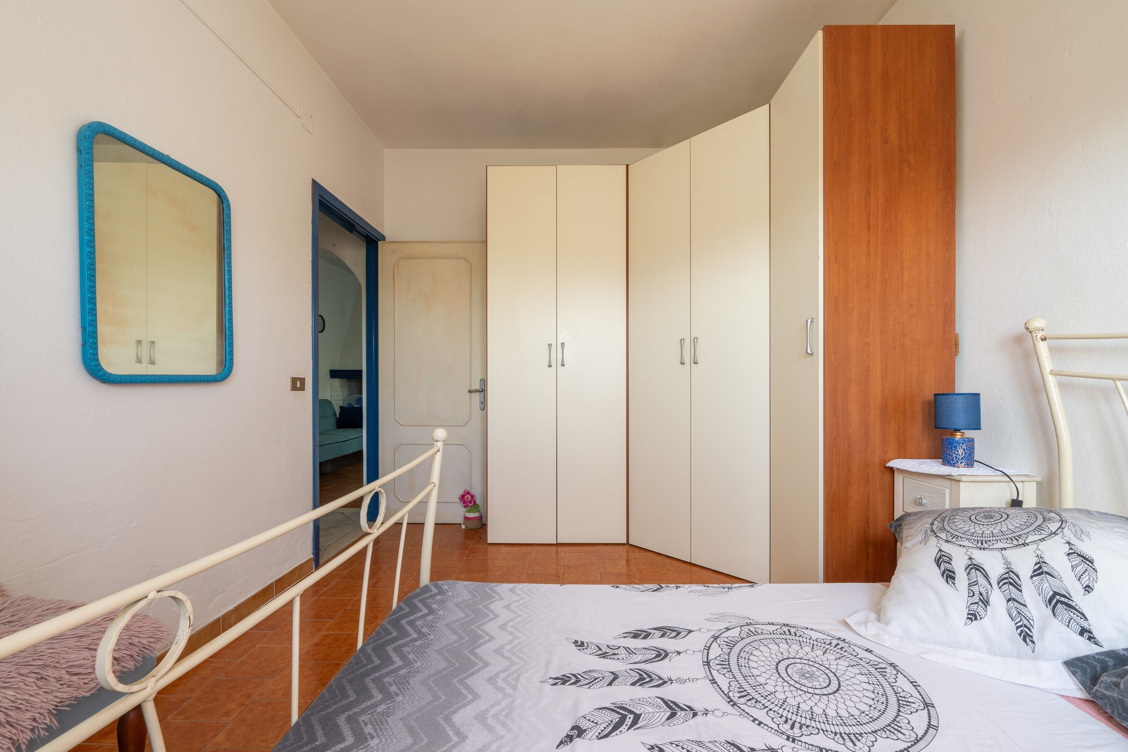 A bedroom with a bed, a wardrobe, a bedside table with a lamp, and a mirror on the wall.