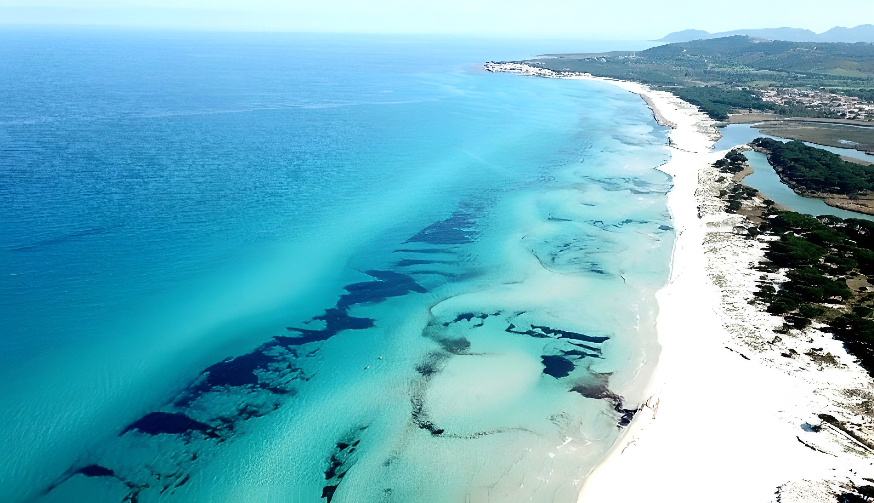 Eine Luftaufnahme einer Küstenregion mit Strand, klarem blauen Wasser und einer Stadt im Hintergrund.