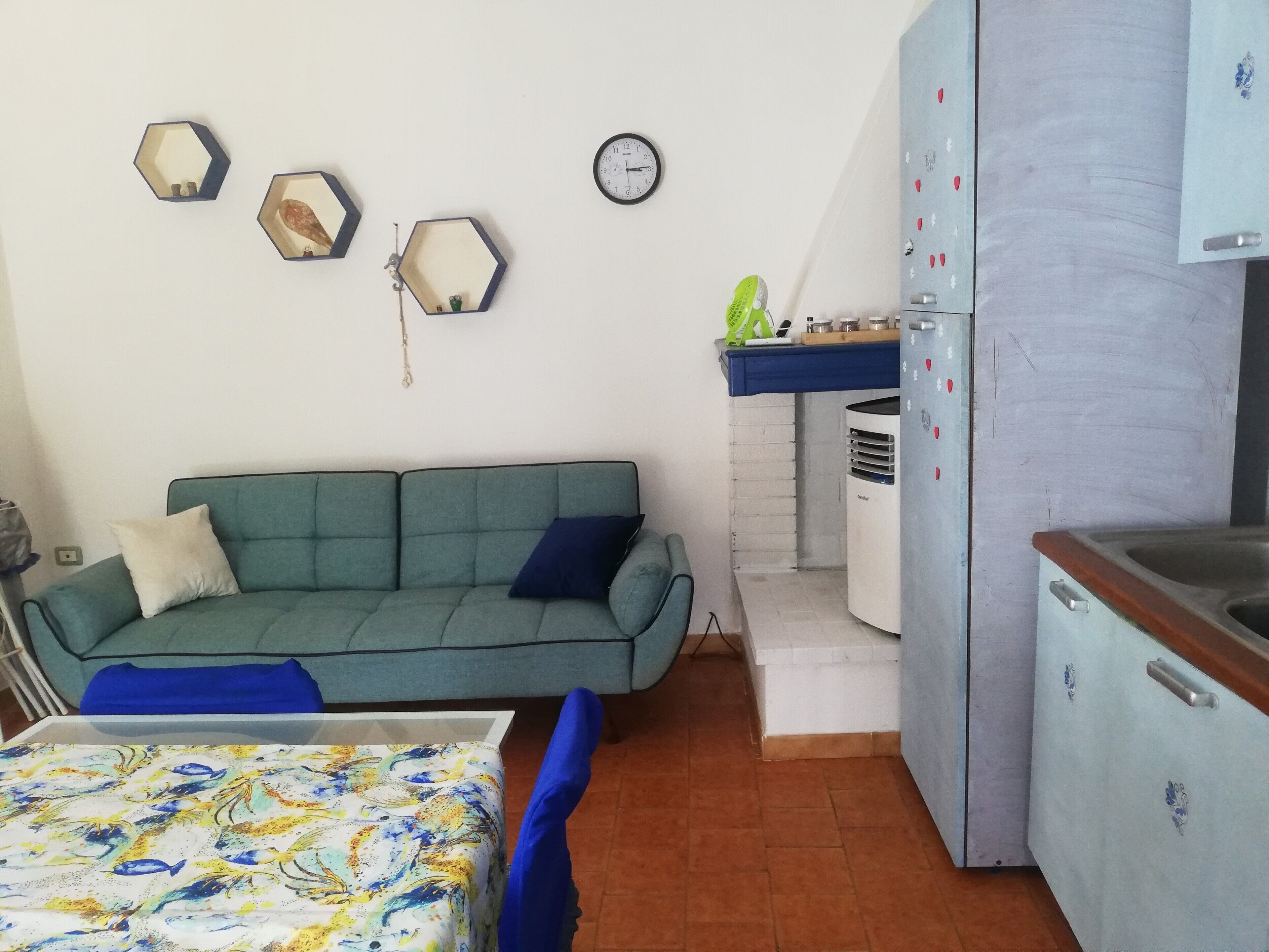 Ein gemütlicher Wohnraum mit Sofa, einer kleinen Küchenzeile und einem Bett mit bunter Bettdecke.