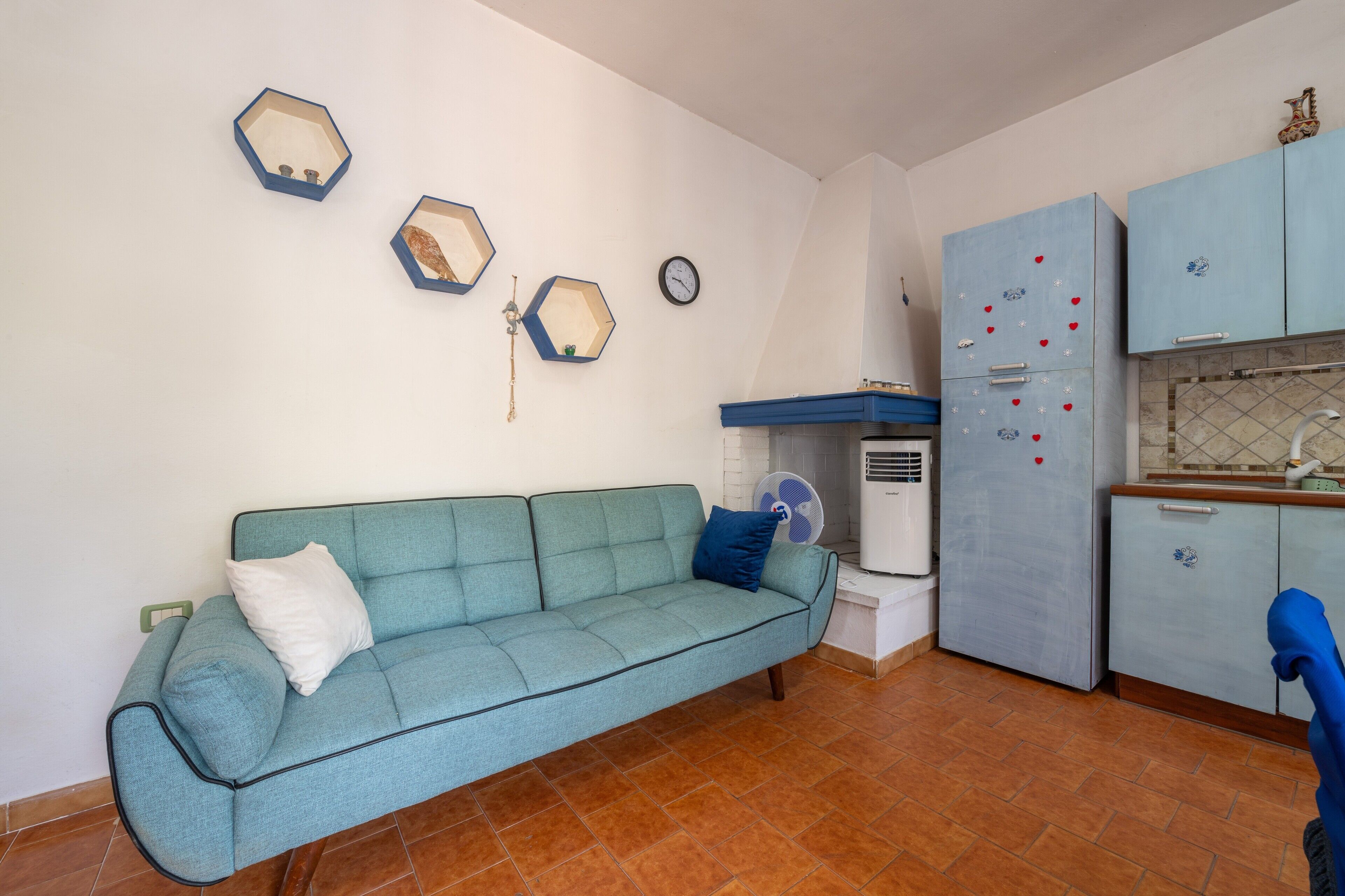 Un espace de vie compact comprenant un canapé, une kitchenette et une horloge murale.