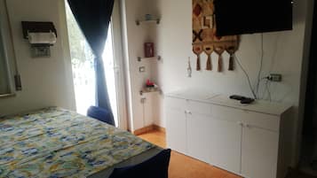 Une chambre à coucher avec un lit, un bureau, une télévision et une fenêtre avec des rideaux.
