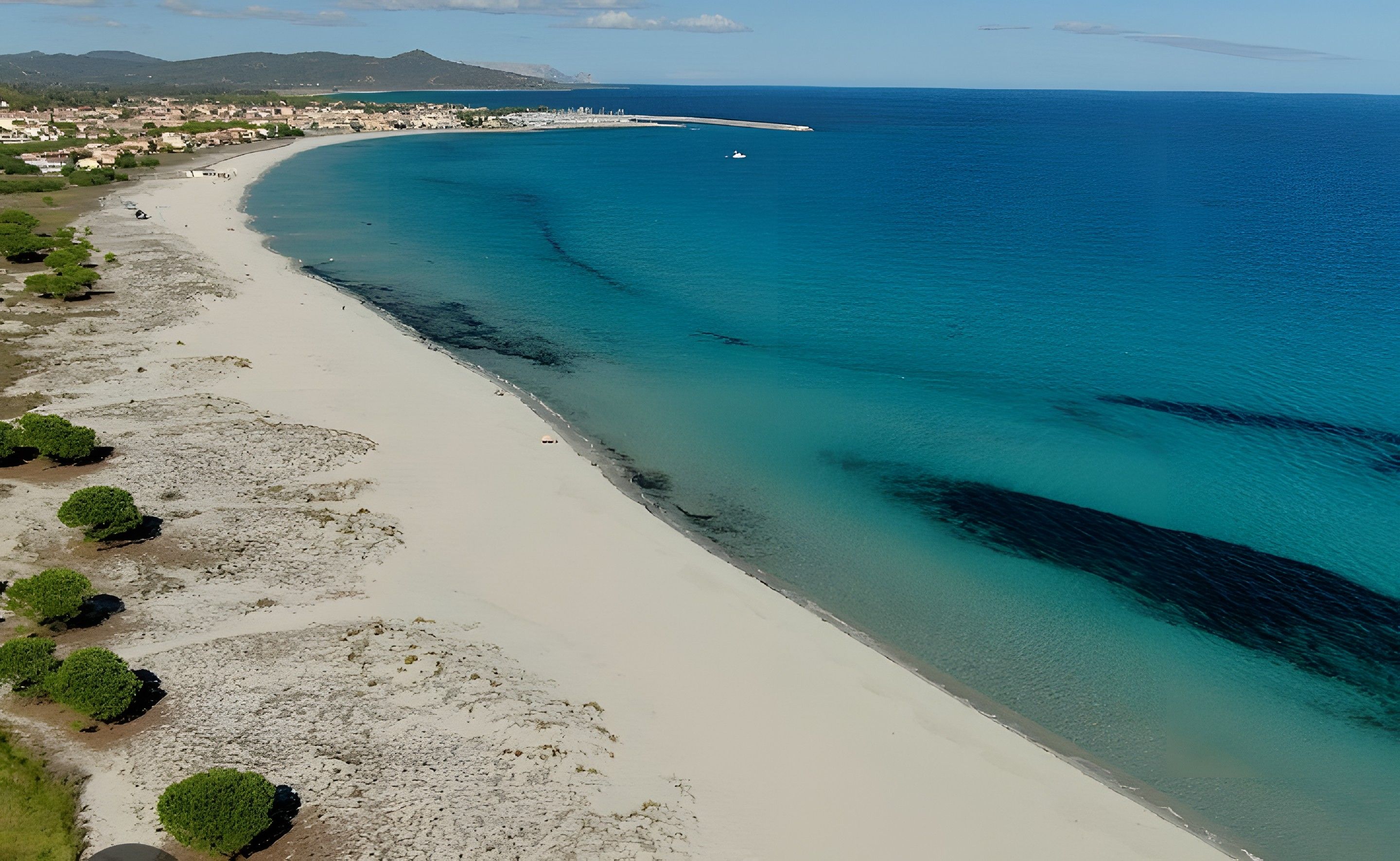 Un paysage côtier avec une plage de sable, des eaux bleues et limpides, et une côte lointaine parsemée de bâtiments.