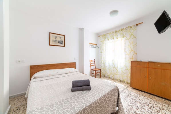 A bedroom with a bed, a wooden headboard, a wardrobe, a chair, a picture on the wall, and a TV mounted on the wall.