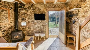 A stone-walled room with a fireplace, wooden furniture, a television, and a view of the outdoors. - Apartment 'La Rústica' with Mountain View, Shared Garden and Wi-Fi (susqueda)