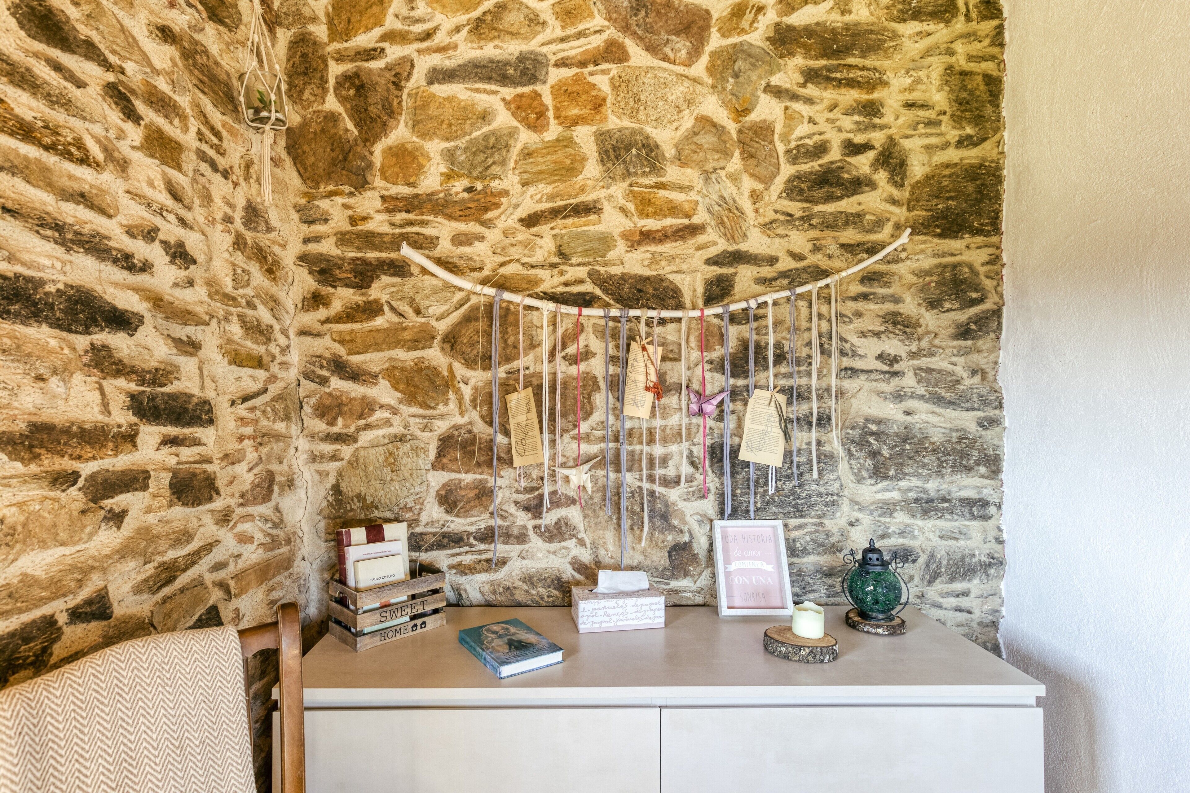 Un muro de piedra, un aparador blanco con libros, una vela y un farol verde.