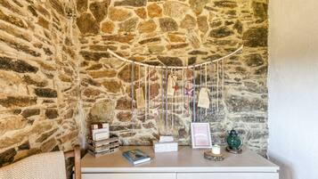 Un muro de piedra, un aparador blanco con libros, una vela y un farol verde.