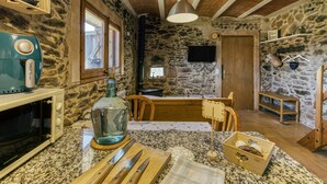 A rustic kitchen with a stone wall, wooden ceiling, a vintage microwave, a large bottle, and a wooden table. - Apartment 'La Rústica' with Mountain View, Shared Garden and Wi-Fi (susqueda)