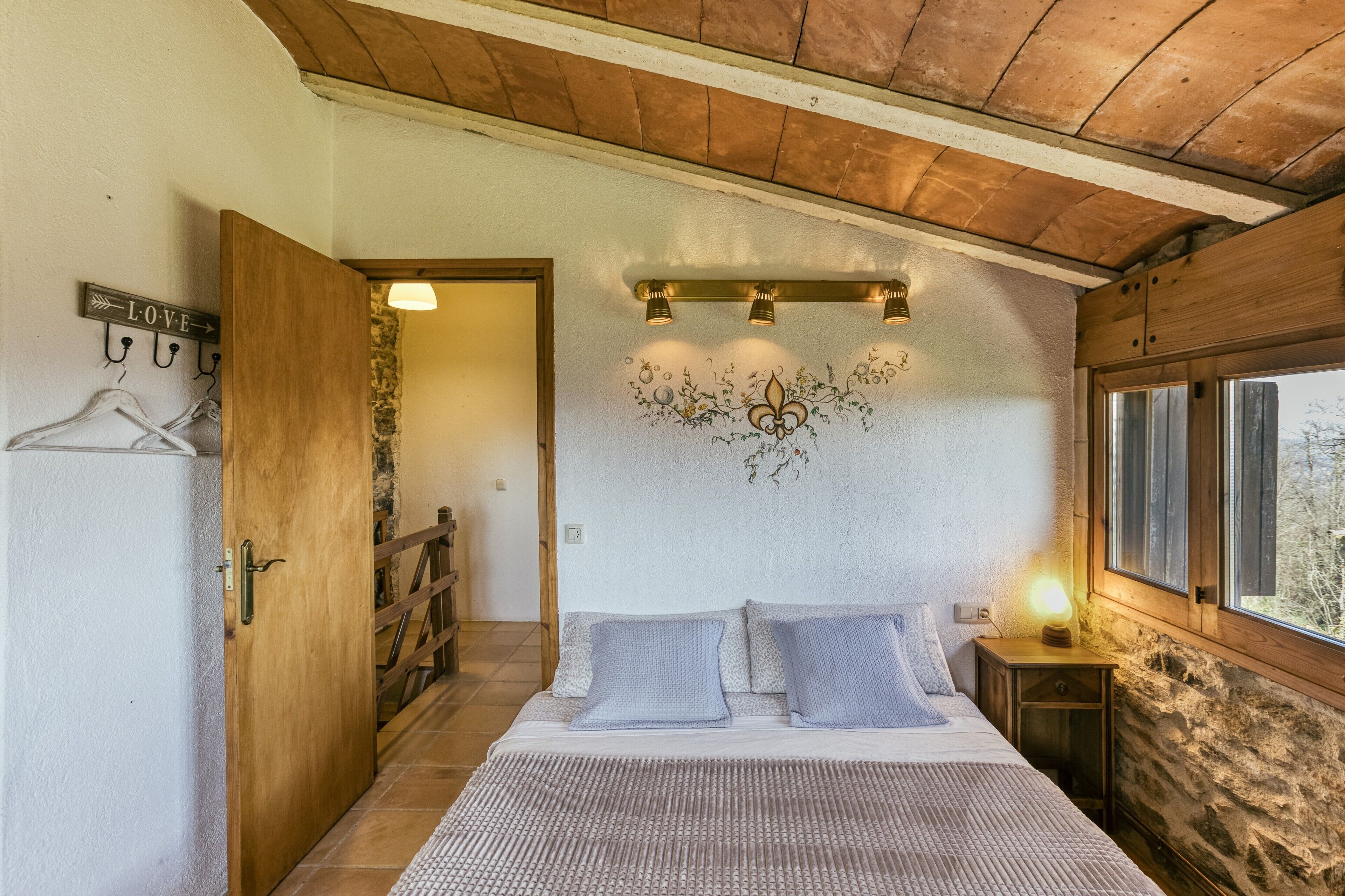 Une chambre à coucher avec un lit, une porte en bois, un luminaire fixé au mur et une fenêtre.