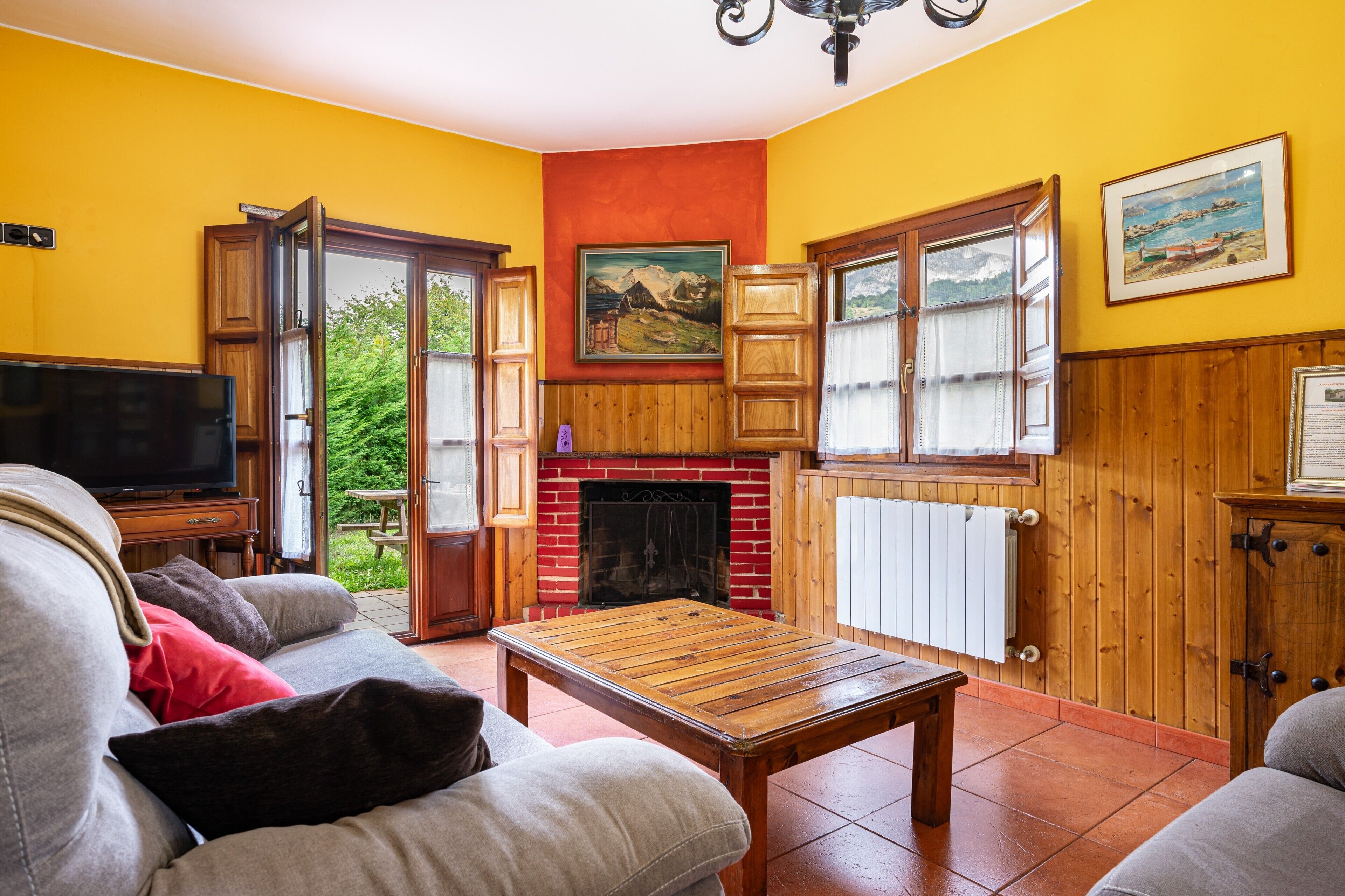 Ein Wohnzimmer mit Fernseher, einer Couch, einem Holztisch, einem Kamin und großen Fenstern.