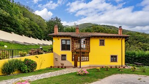 A yellow building with a balcony, surrounded by greenery and a stone pathway.