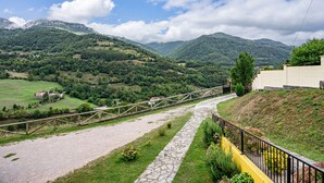 A rural landscape with a stone pathway, a wooden fence, and a building with a yellow wall.