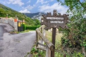 A rustic wooden sign with 'Apartamentos Socastillo' written on it, a wooden fence, and a road leading to a building with a yellow roof. - Country House 'Socastillo C' with Mountain View, Private Terrace and Private Garden (Quirós)