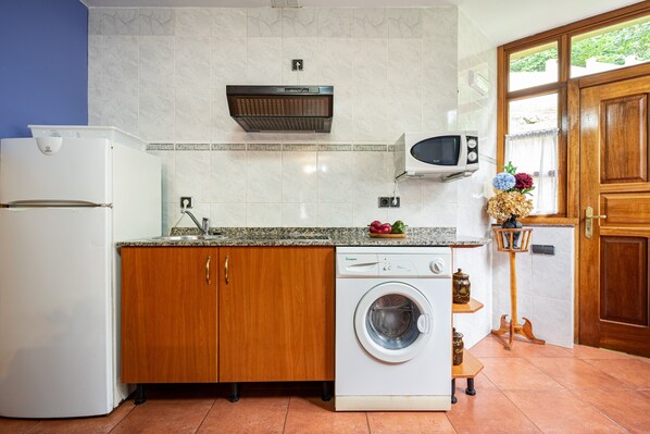 A kitchen with a washing machine, microwave, and wooden cabinets.