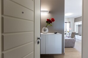 Un intérieur moderne avec une porte blanche, un meuble sur lequel est posé un vase de fleurs rouges, et un coin repas à l’arrière-plan.