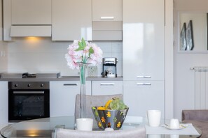 A modern kitchen with white cabinets, a glass table, and a vase with flowers. - Apartment 'La Casa Di Fonte' with Private Terrace, Wi-Fi and Air Conditioning (Fonte Laurentina)