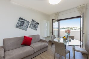Un salon moderne avec un canapé, une table en verre et des chaises, un balcon avec vue et deux œuvres d’art abstraites accrochées au mur.