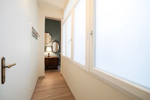 Un couloir doté d’un plancher en bois, d’une porte avec une poignée en laiton, d’un luminaire fixé au mur et d’un miroir.