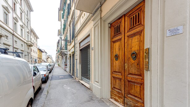 A narrow street with parked cars and a large wooden door on the right.