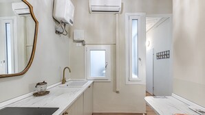 A modern bathroom with a marble countertop, a gold faucet, a small window, and a white door.