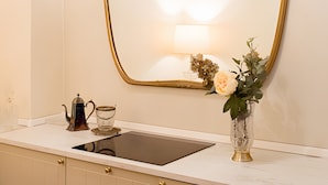 A bathroom with a white countertop, a gold-framed mirror, a chandelier, a vase with flowers, and a kettle.