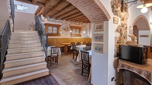 Un interior rústico con una escalera, vigas de madera, paredes de piedra y un comedor con mesas y sillas.