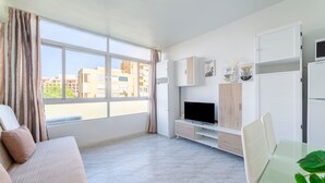 Ein modernes Wohnzimmer mit einer Couch, einem Fernseher, einem Glastisch und weißen Schränken.