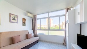 Ein Zimmer mit einer Couch, einem Fernseher, einem Fenster und Bildern an der Wand.