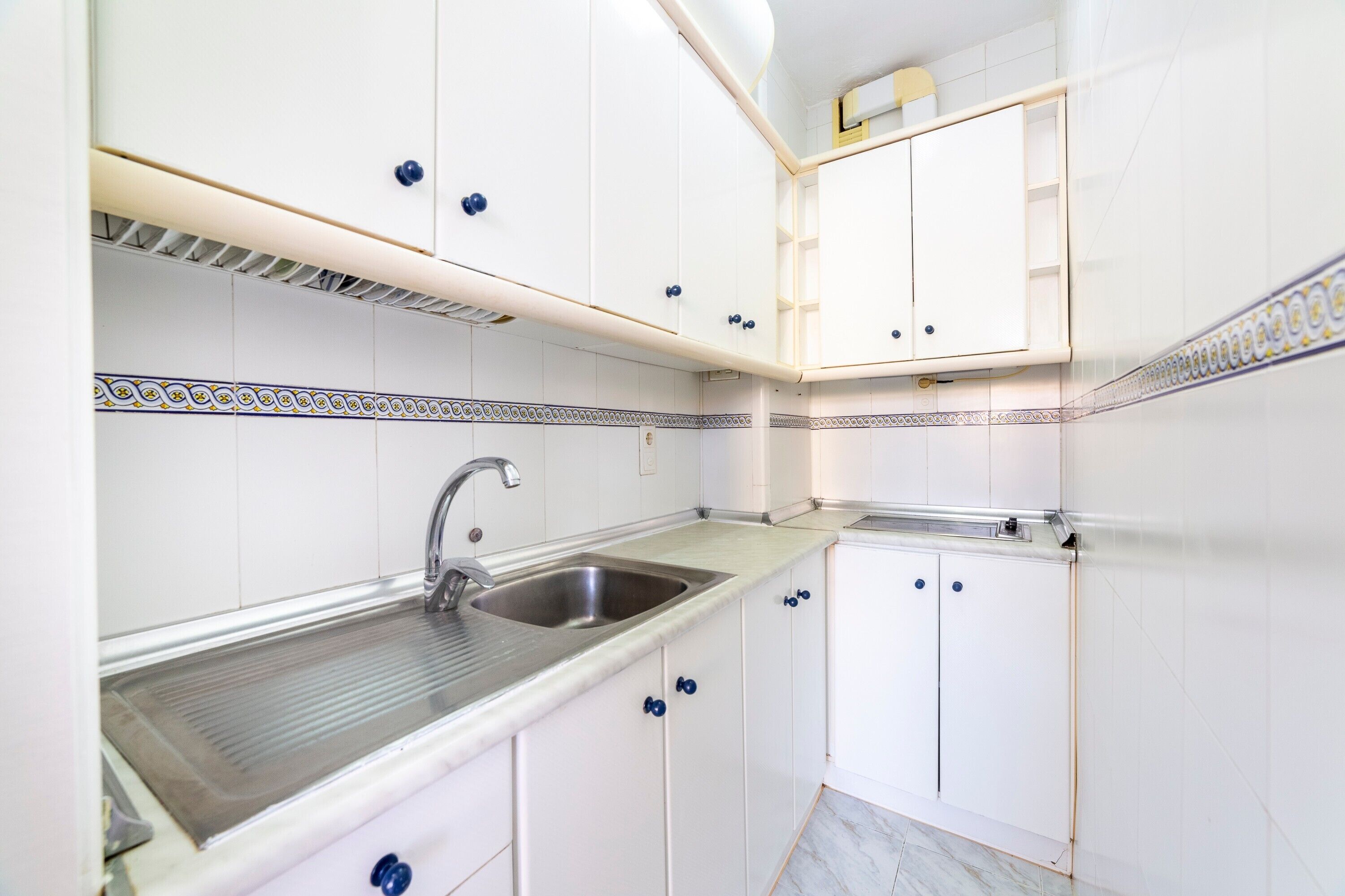 Cocina con gabinetes blancos, pileta de acero inoxidable y salpicadero de azulejos estampados.