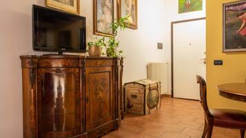 A room with a wooden cabinet, a television, a potted plant, a suitcase, and a dining table with a chair.