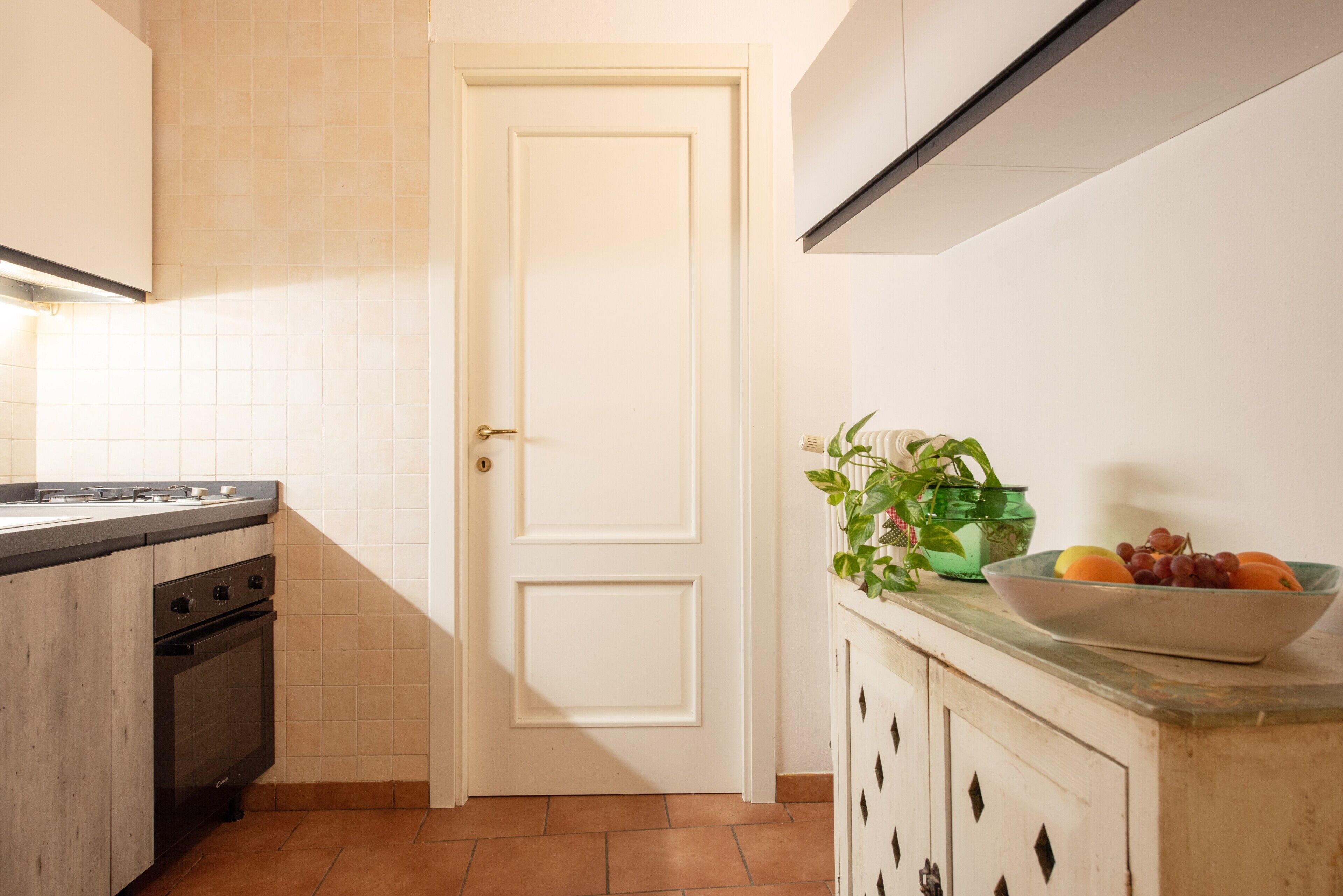 Una cocina con estufa, horno, una puerta blanca y un bol de fruta en la encimera.