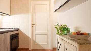 Una cocina con estufa, horno, una puerta blanca y un bol de fruta en la encimera.